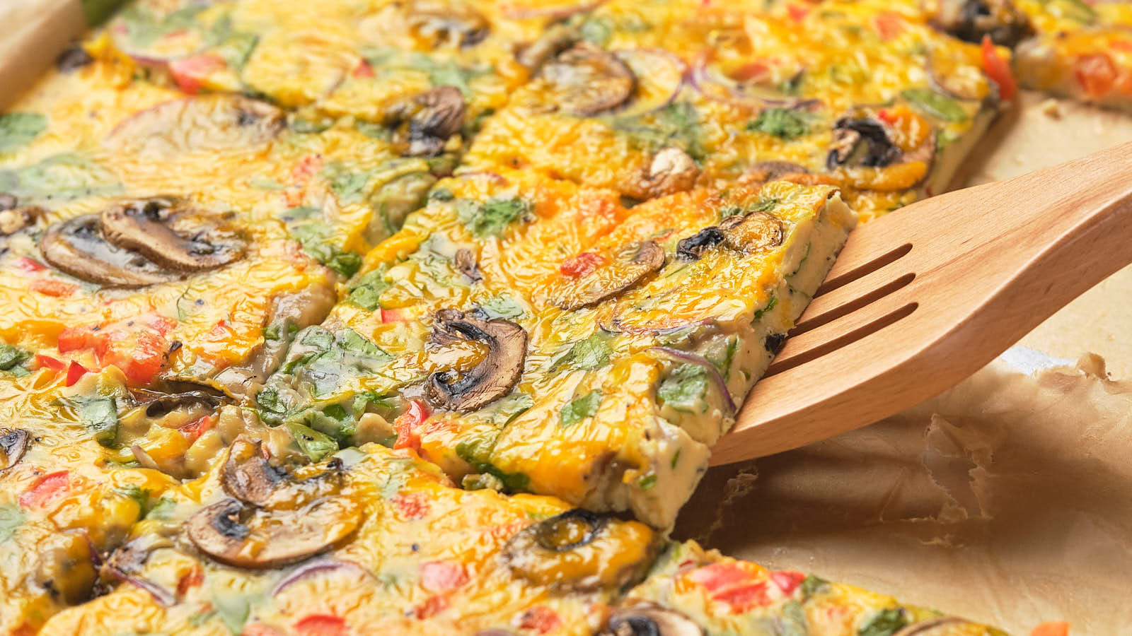 Sheet pan eggs cut into squares, featuring sliced mushrooms, bell peppers, and greens.