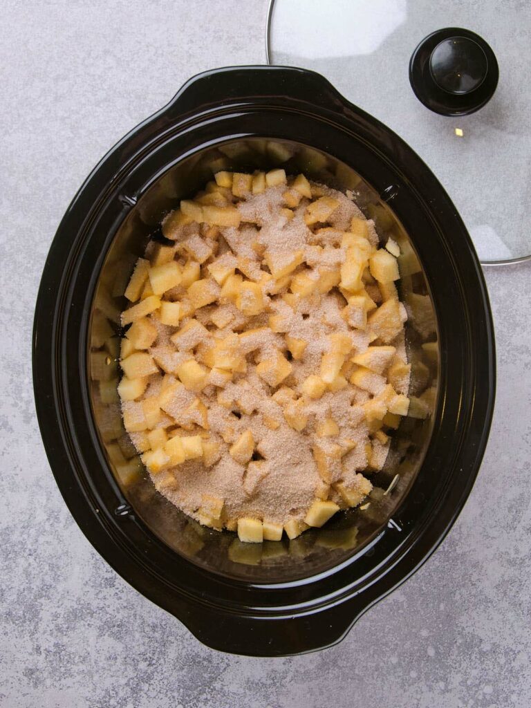 Slow cooker filled with chopped apples and sugar, viewed from above.