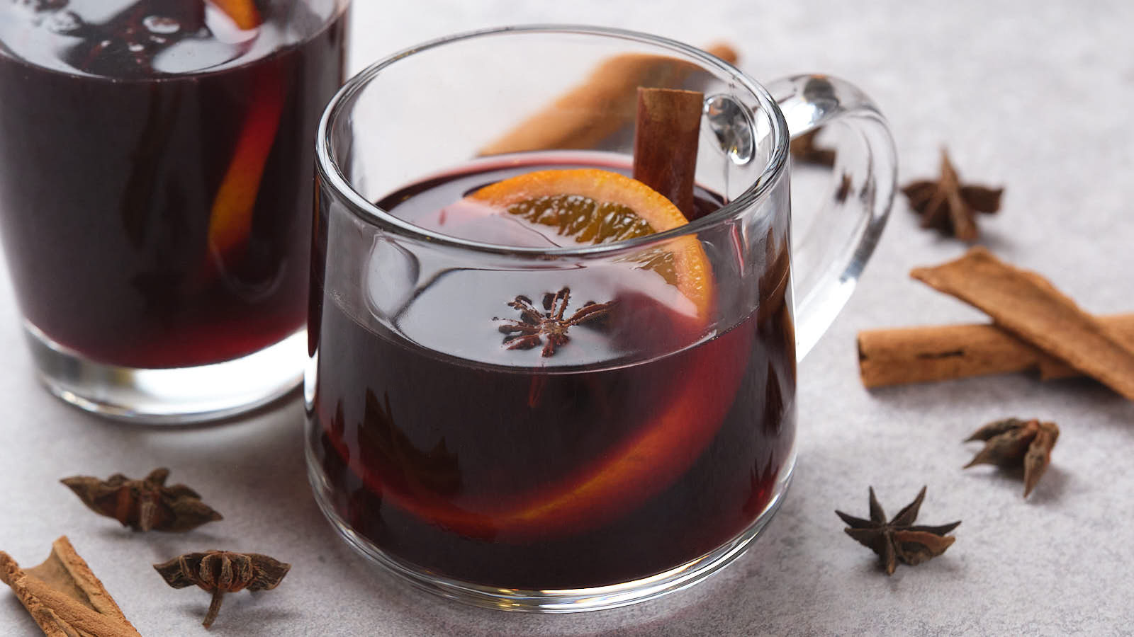 Two clear glass mugs of mulled wine with orange slices, star anise, and cinnamon sticks.