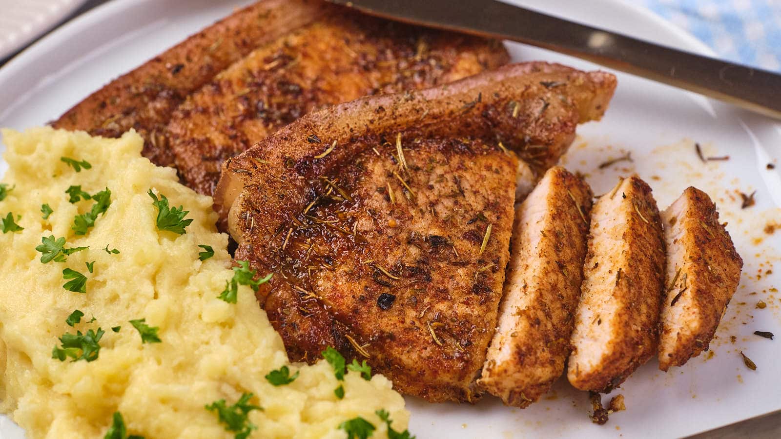 A serving of seasoned pork chops with a side of mashed potatoes on a white plate.