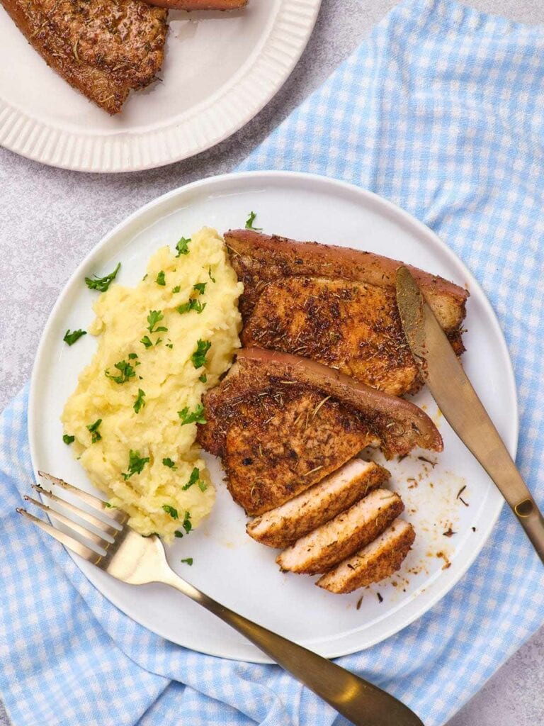 Pork chops on a white plate with a side of mashed potatoes.