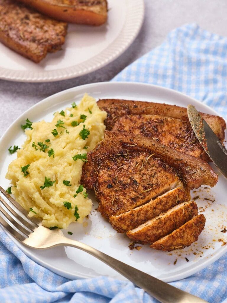 A white plate containing a serving of pork chops and mashed potatoes.