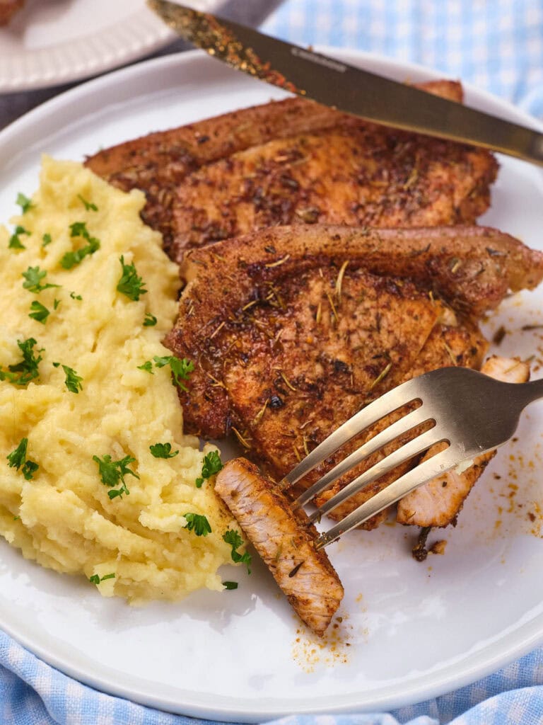 A serving of pork chops with mashed potatoes on a white plate with knife and fork .