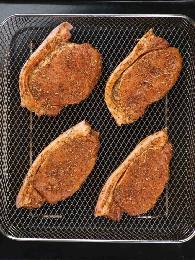 Four seasoned pork chops are arranged on a wire rack, ready for grilling or baking.