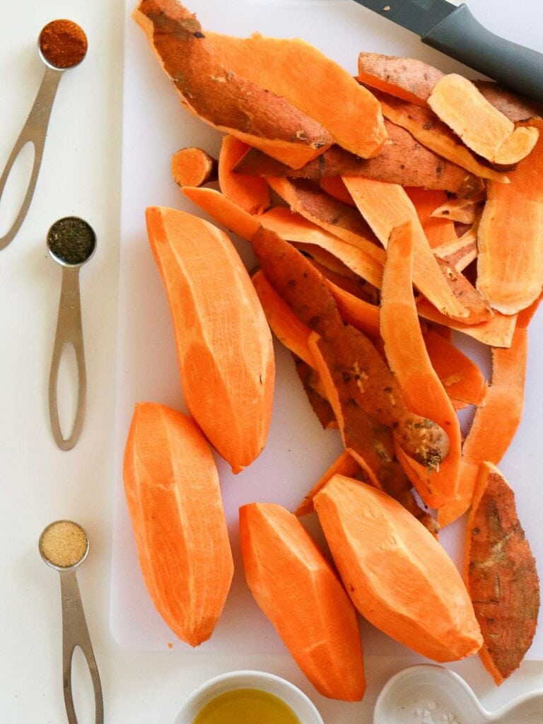 Peeled sweet potatoes and peels on a cutting board.