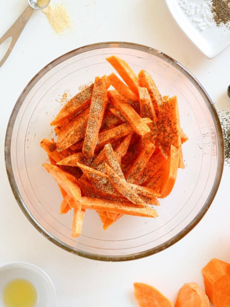 A bowl of uncooked sweet potato fries seasoned with herbs and spices.