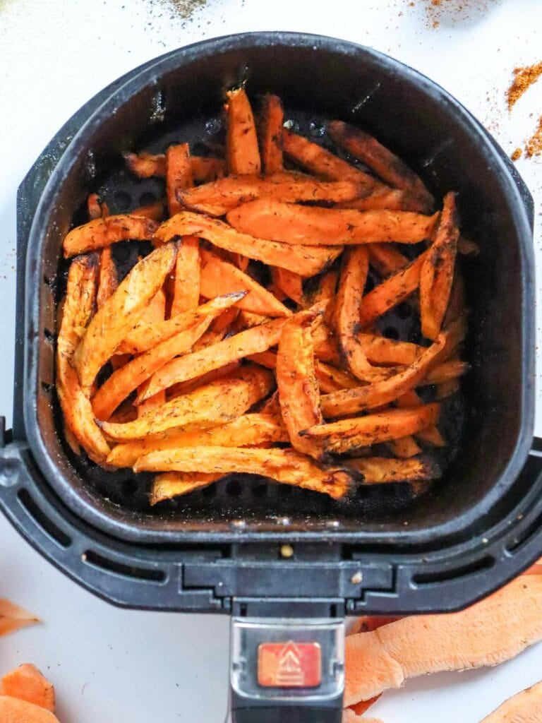 Sweet potato fries seasoned and cooked in an air fryer basket.