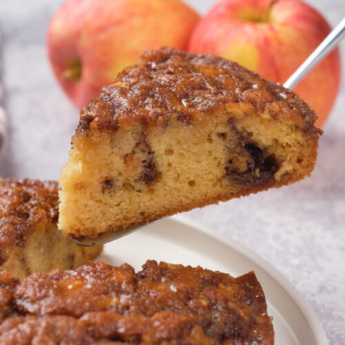 A slice of apple upside-down apple cinnamon cake with a caramelized top is lifted from a plate.