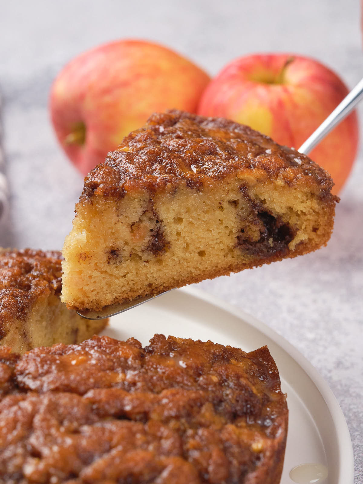 A slice of apple upside-down apple cinnamon cake with a caramelized top is lifted from a plate.