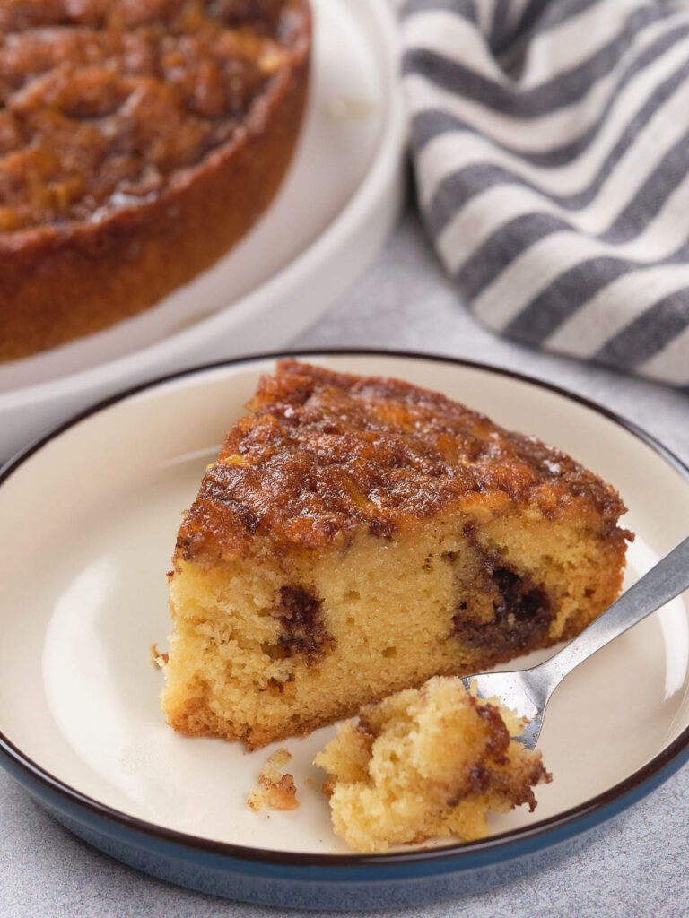 A slice of apple cinnamon cake with visible cinnamon swirl, served on a plate, with a fork holding a bite.