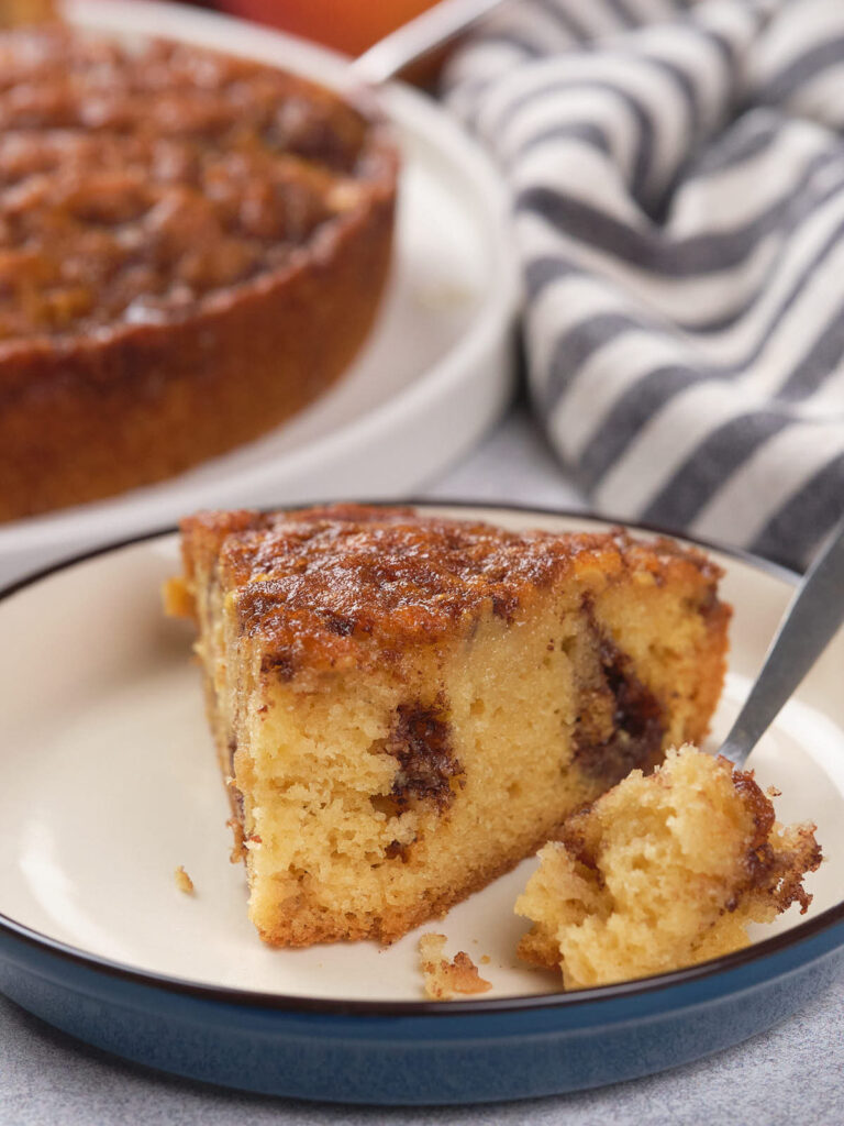 A slice of apple cinnamon cake on a plate, with a fork taking a piece.