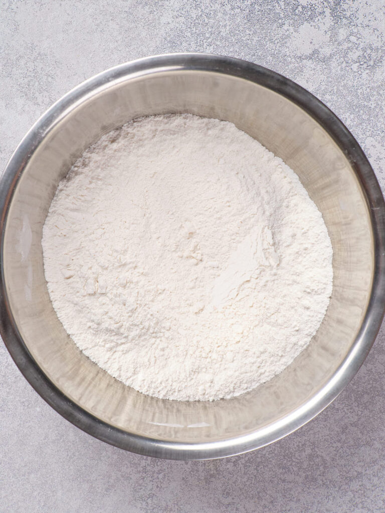 A stainless steel bowl filled with white flour on a gray surface.