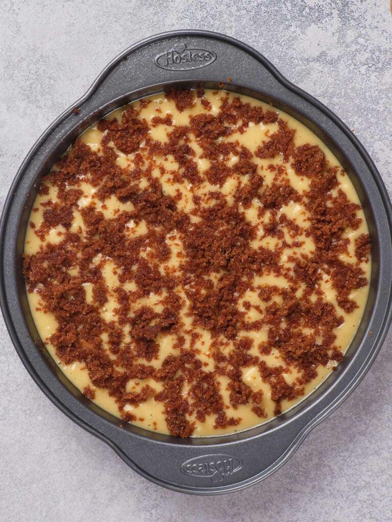 Round cake pan filled with a cream-colored dessert topped with crumbled brown bits.