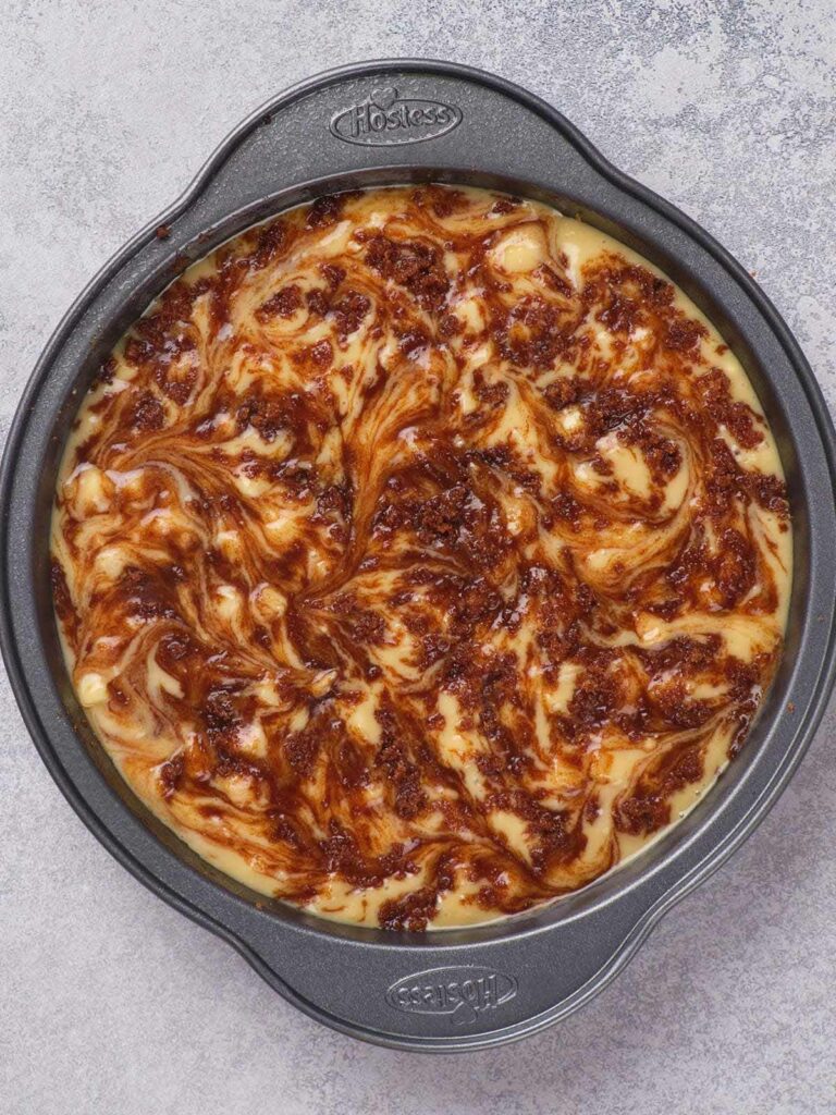 A round cake pan filled with batter swirled with chocolate and caramel.