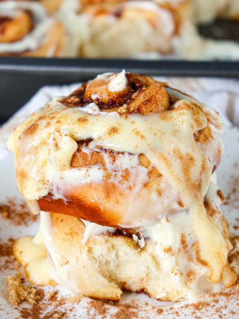 Close-up of a cinnamon roll drizzled with icing and sprinkled with cinnamon, sitting on a white plate.