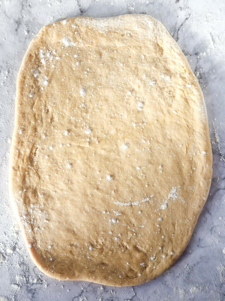 A rolled-out dough on a floured marble surface.