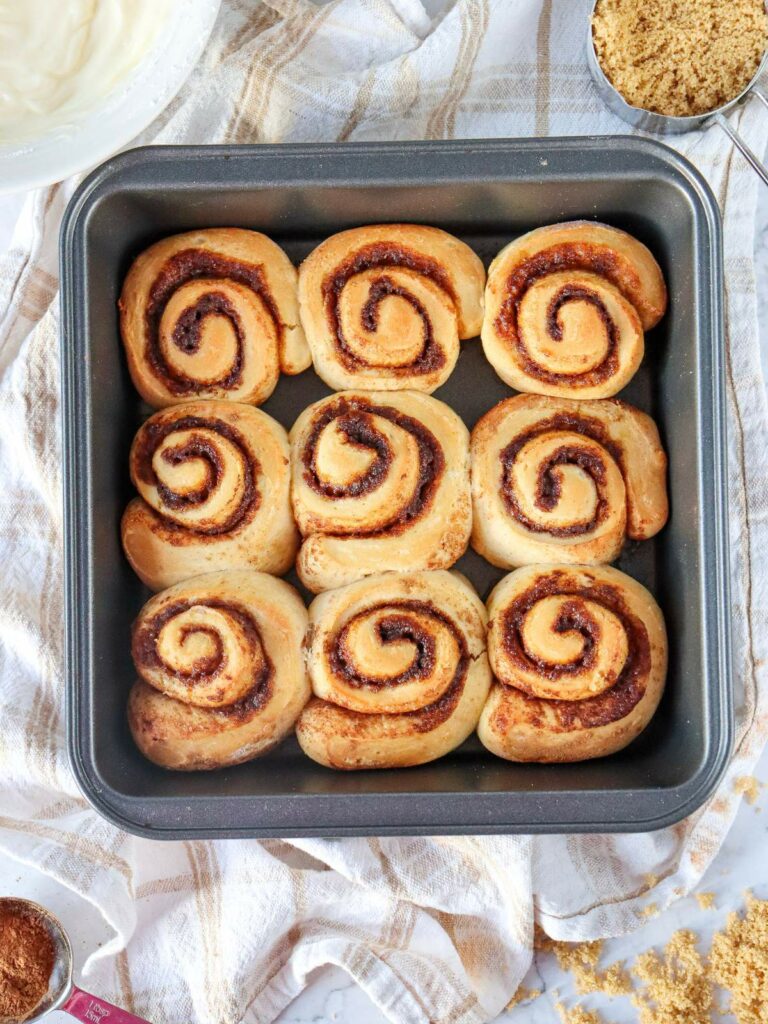 A tray of nine freshly baked cinnamon rolls arranged in three rows.