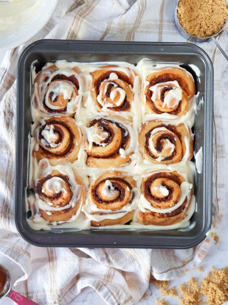 A tray of nine freshly baked cinnamon rolls topped with creamy icing, set on a cloth.