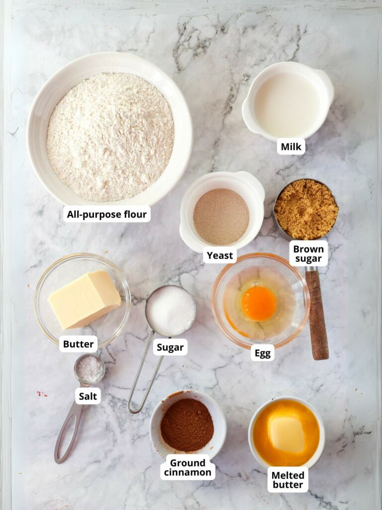 Ingredients for cinnamon rolls arranged on a marble surface.