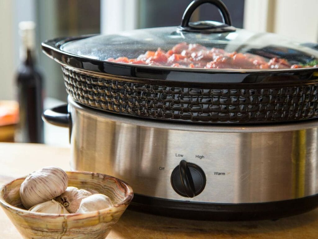 A slow cooker set to low with a glass lid, partially filled with food.