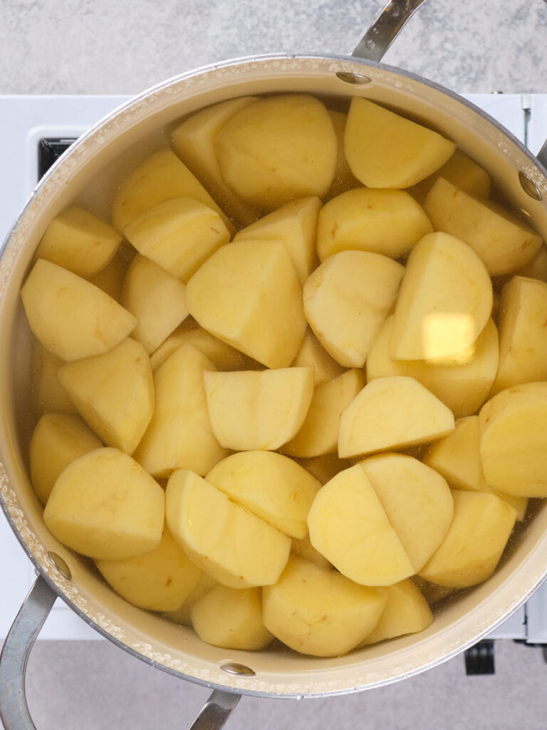 A pot filled with peeled and chopped potatoes submerged in water.