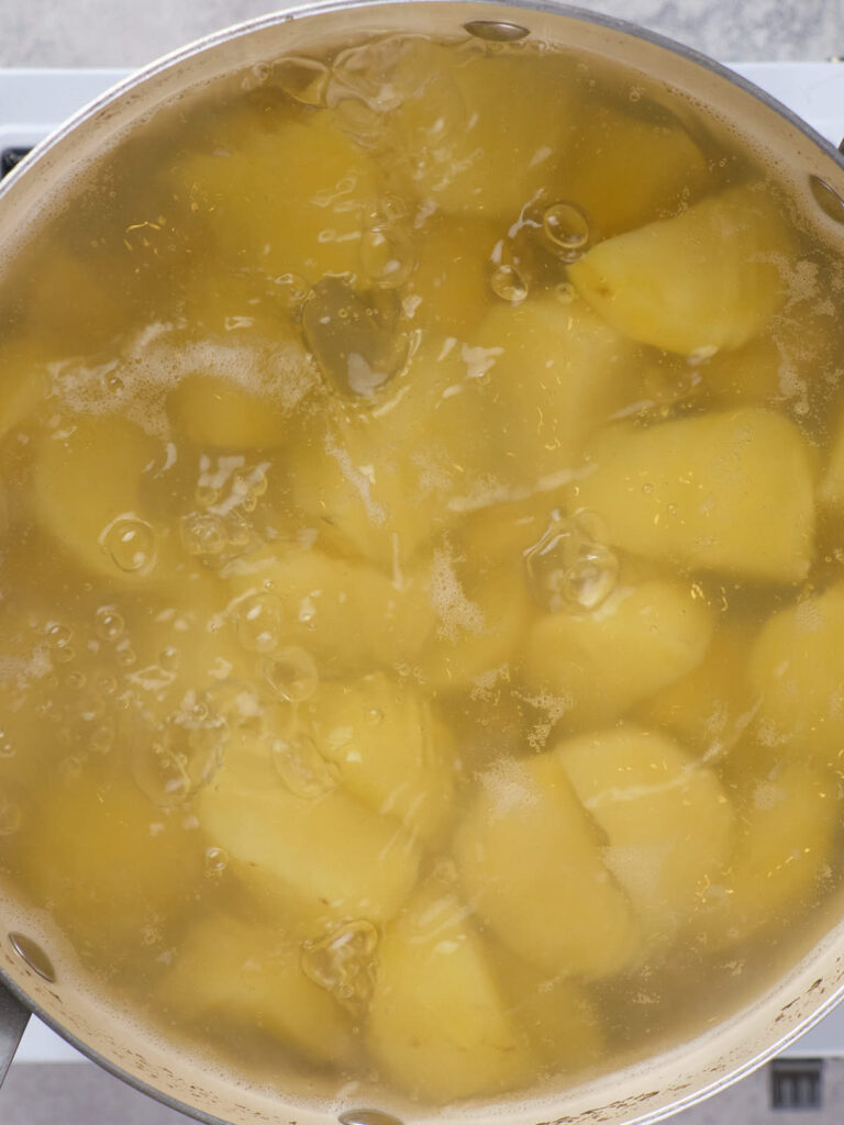 Potatoes boiling in a pot of water on a stovetop.