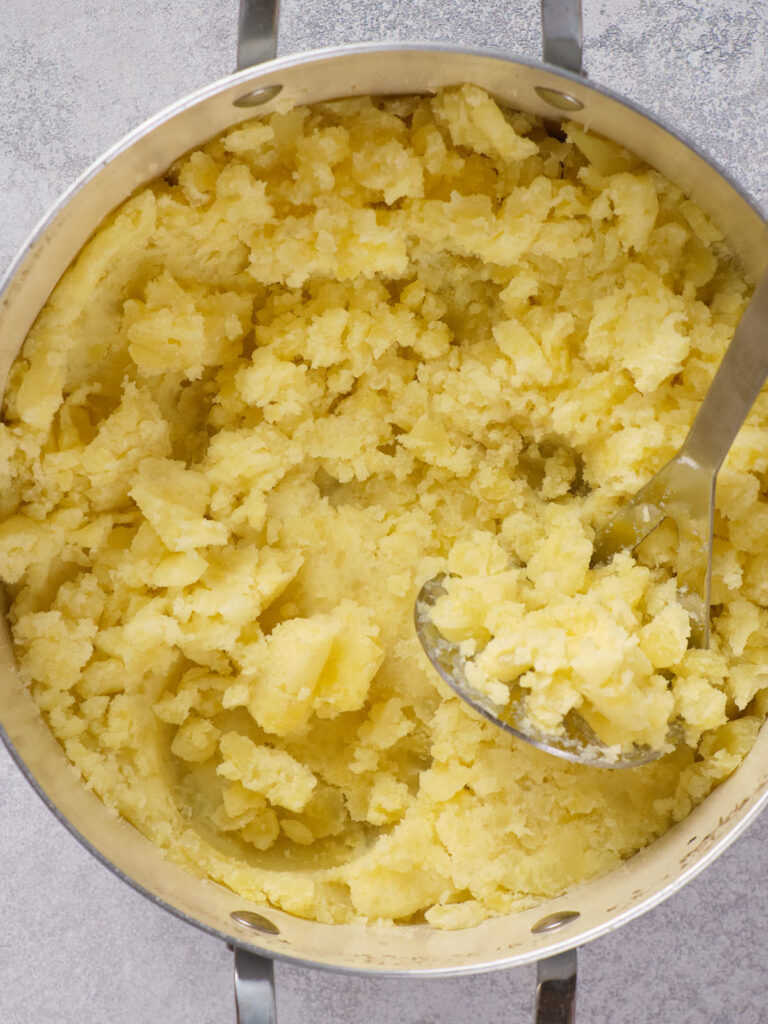 A pot of mashed potatoes with a serving spoon on a gray surface.