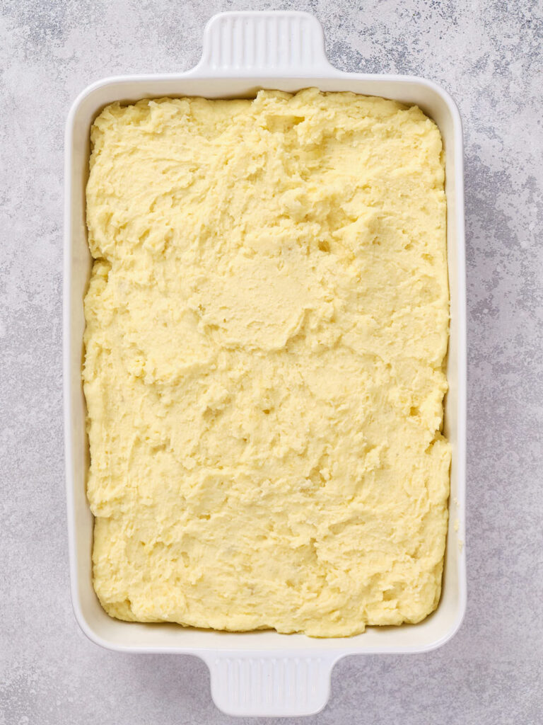 A rectangular white baking dish filled with an even layer of mashed potatoes on a gray speckled surface.