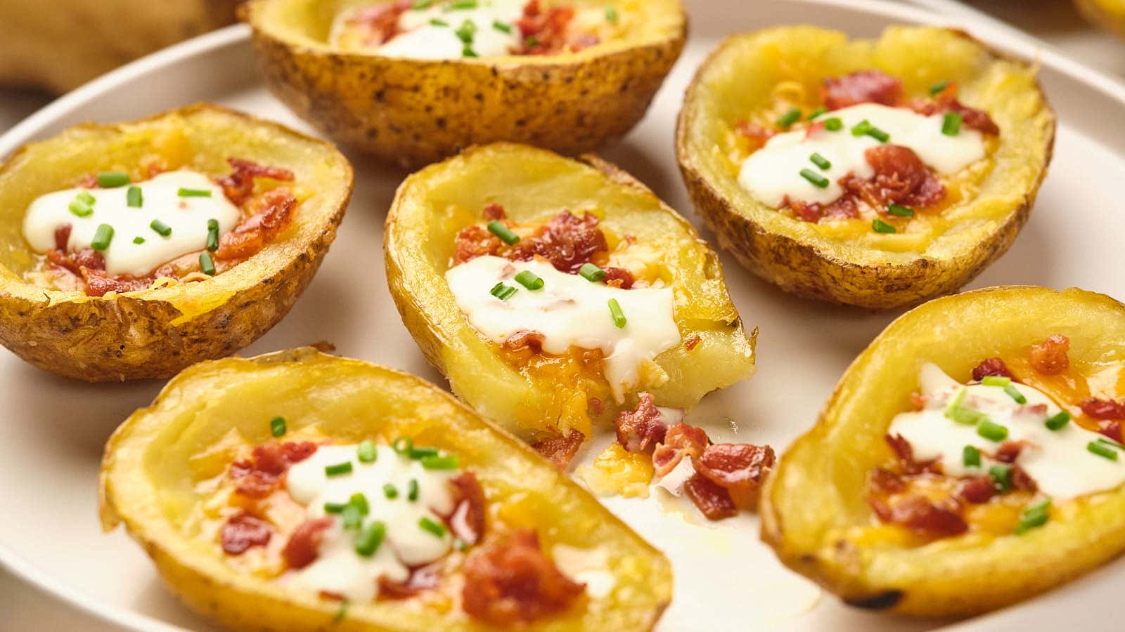 A plate of potato skins topped with melted cheese, crispy bacon bits, sour cream, and chopped chives.