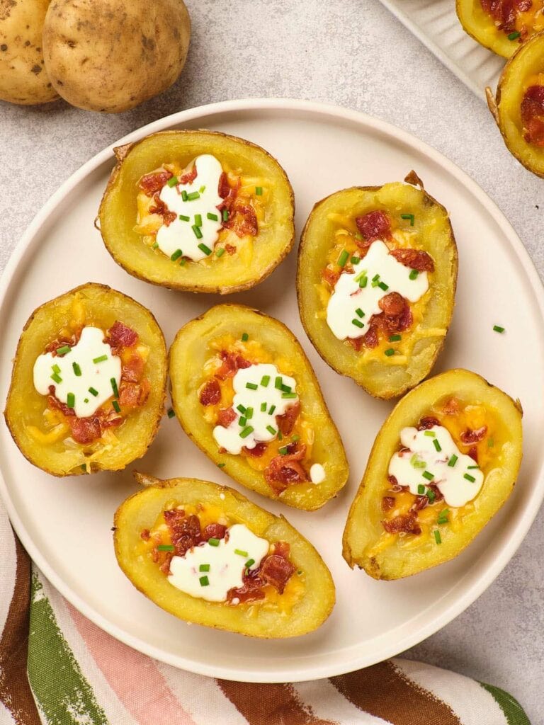 Plate of potato skins topped with melted cheese, bacon bits, sour cream, and chopped chives.