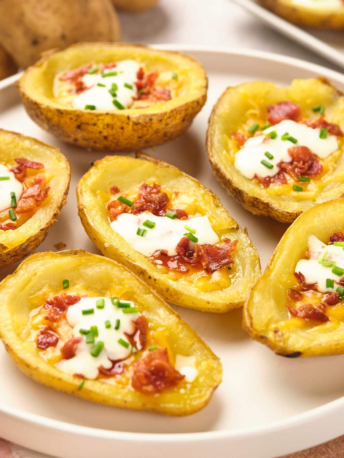 Potato skins topped with sour cream, bacon bits, and chives on a white plate.