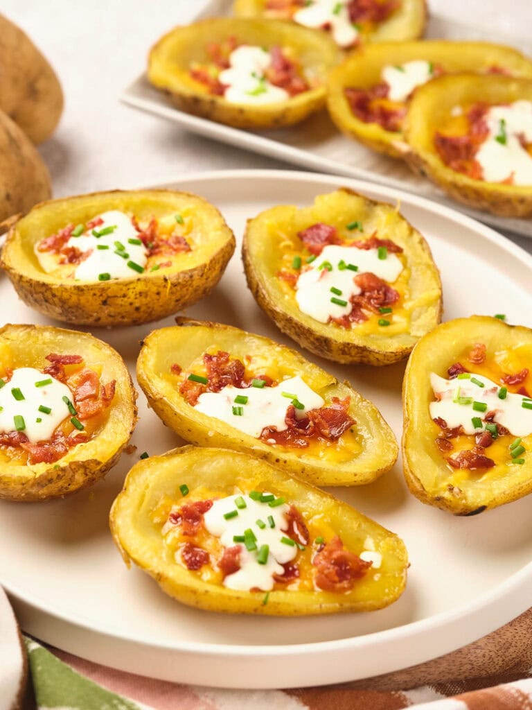 Baked potato skins topped with melted cheese, bacon bits, sour cream, and chives on a white plate.