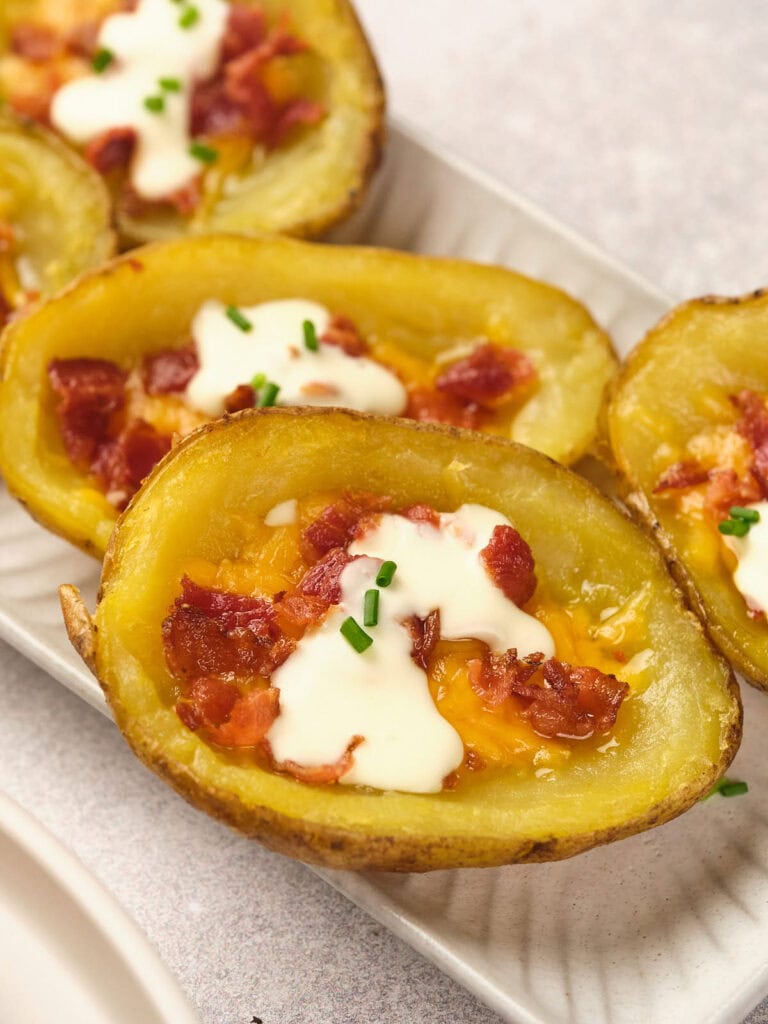 Potato skins topped with melted cheese, bacon, sour cream, and chives on a white plate.