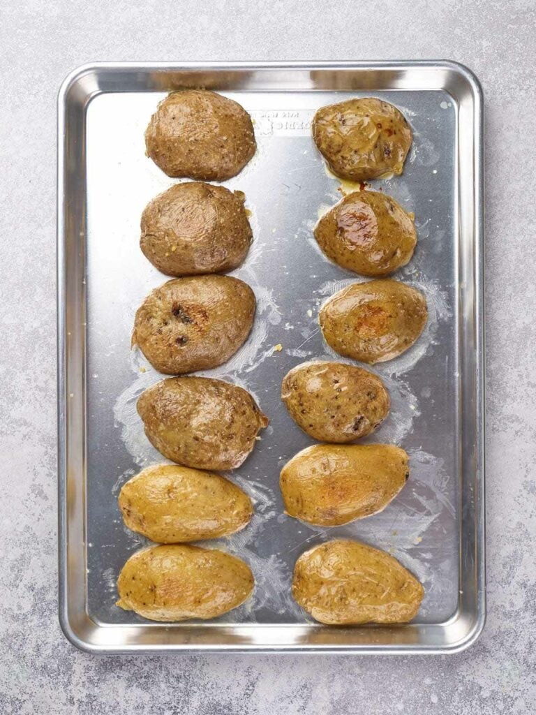 Twelve baked potatoes on a metal baking sheet.