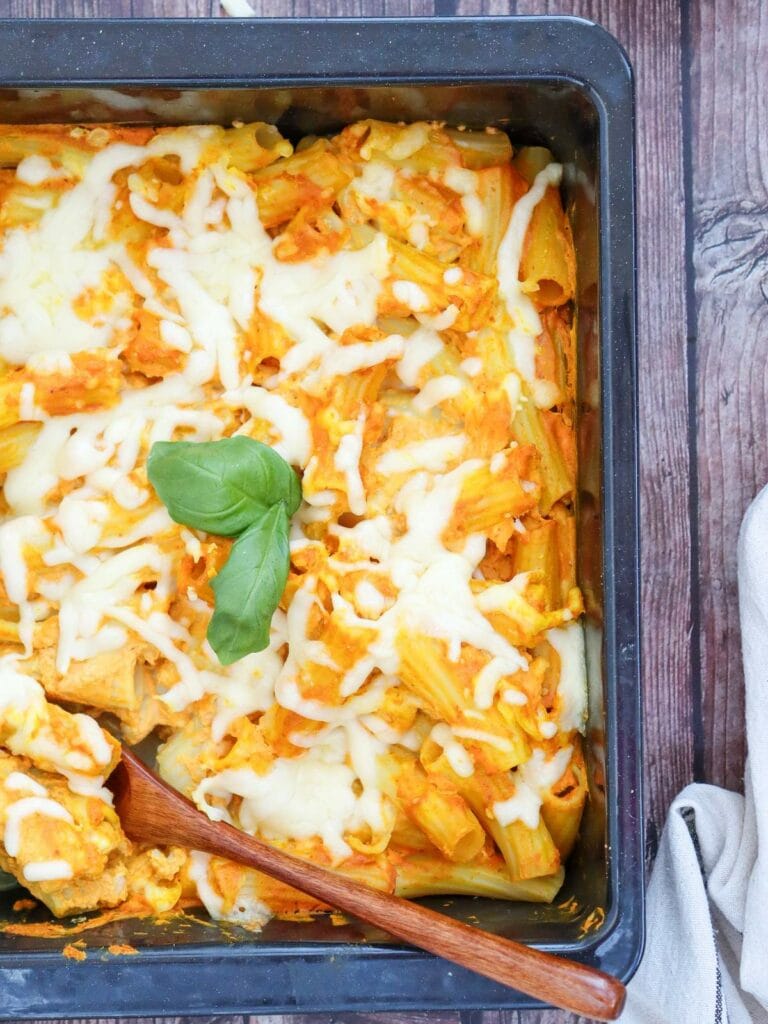 A tray of pumpkin pasta covered in melted cheese and garnished with a basil leaf.