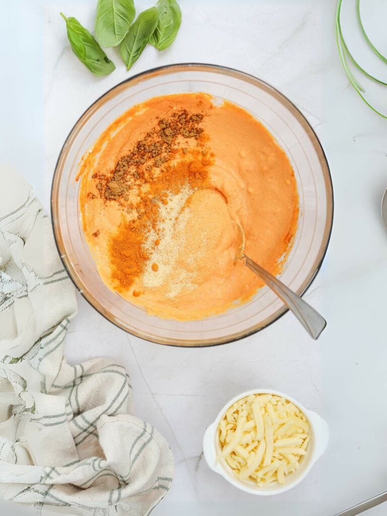 Glass bowl with creamy orange sauce, topped with spices, next to white cheese in a small bowl.