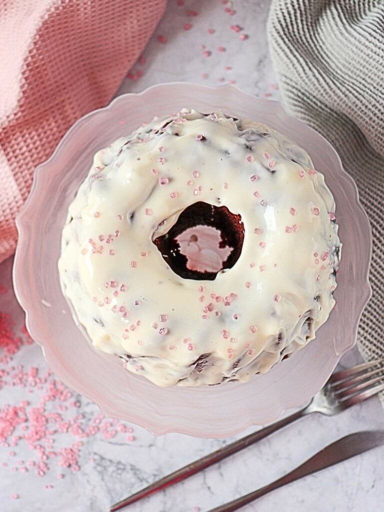 Red velvet cake surrounded by pink and green napkins, with a fork and knife on a marble surface.