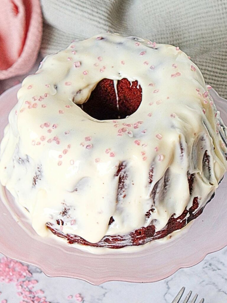 Red velvet cake decorated with pink sugar crystals, sits on a pink plate.