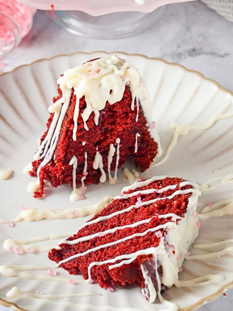 Two slices of red velvet cake with white icing drizzle on a white, scalloped plate.