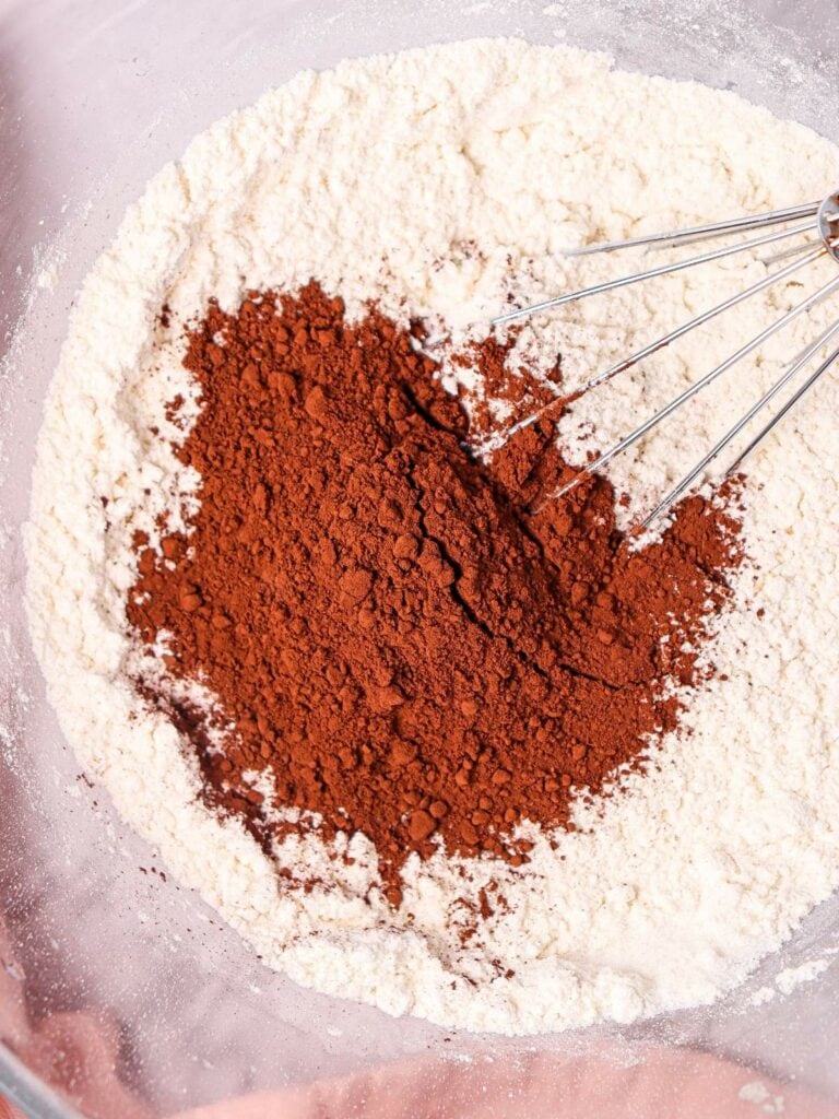 A mixing bowl with flour and cocoa powder. A whisk rests on the edge.