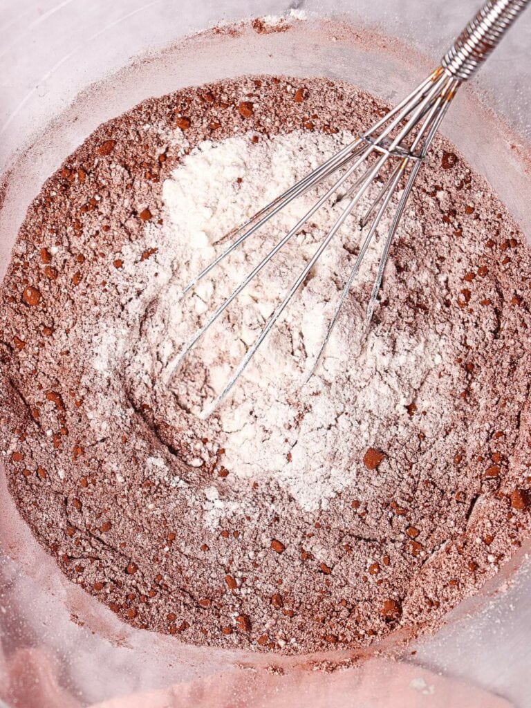 A metal whisk in a bowl with cocoa powder, flour, and sugar mixed together.