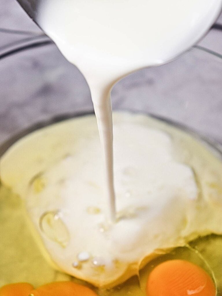 Milk being poured into a bowl containing cracked eggs.