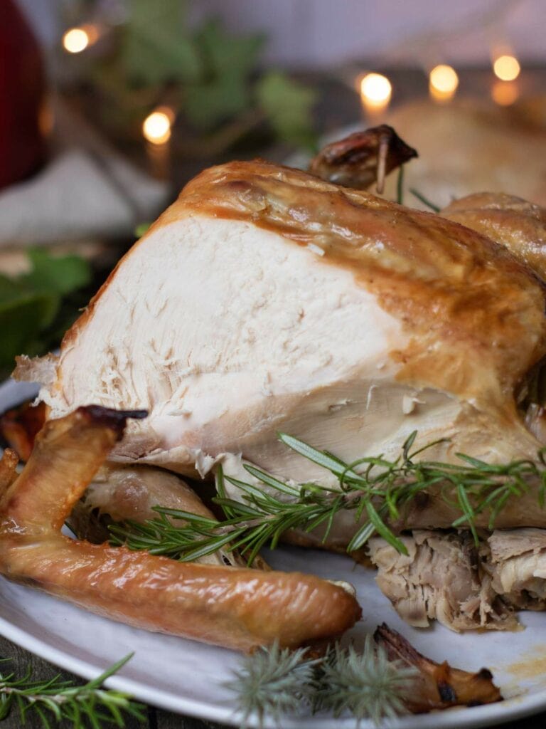 A roasted turkey with a golden-brown exterior is garnished with rosemary sprigs on a serving plate.