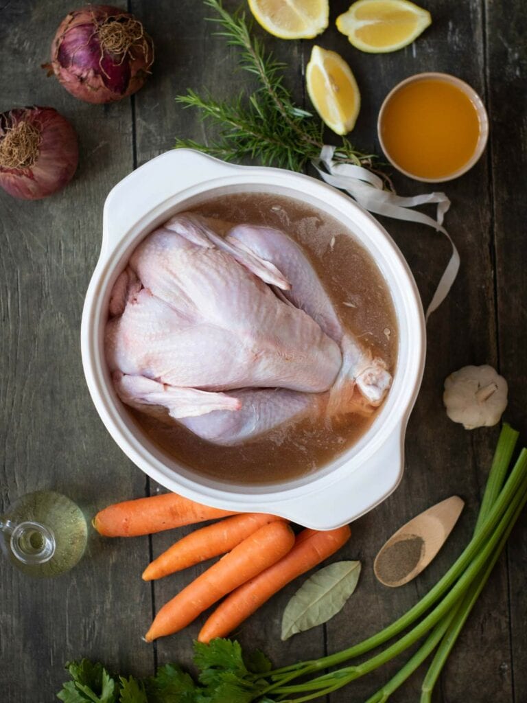 Raw chicken in a pot with broth on a wooden table.