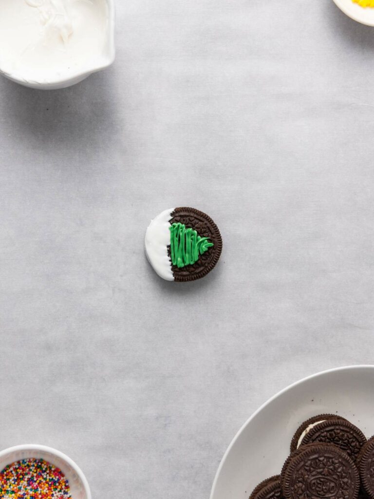 An Oreo cookie half-dipped in white frosting with a green tree design.