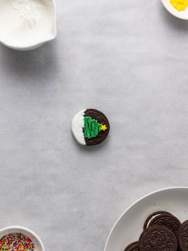 A chocolate sandwich cookie decorated with white icing and a green icing Christmas tree design.