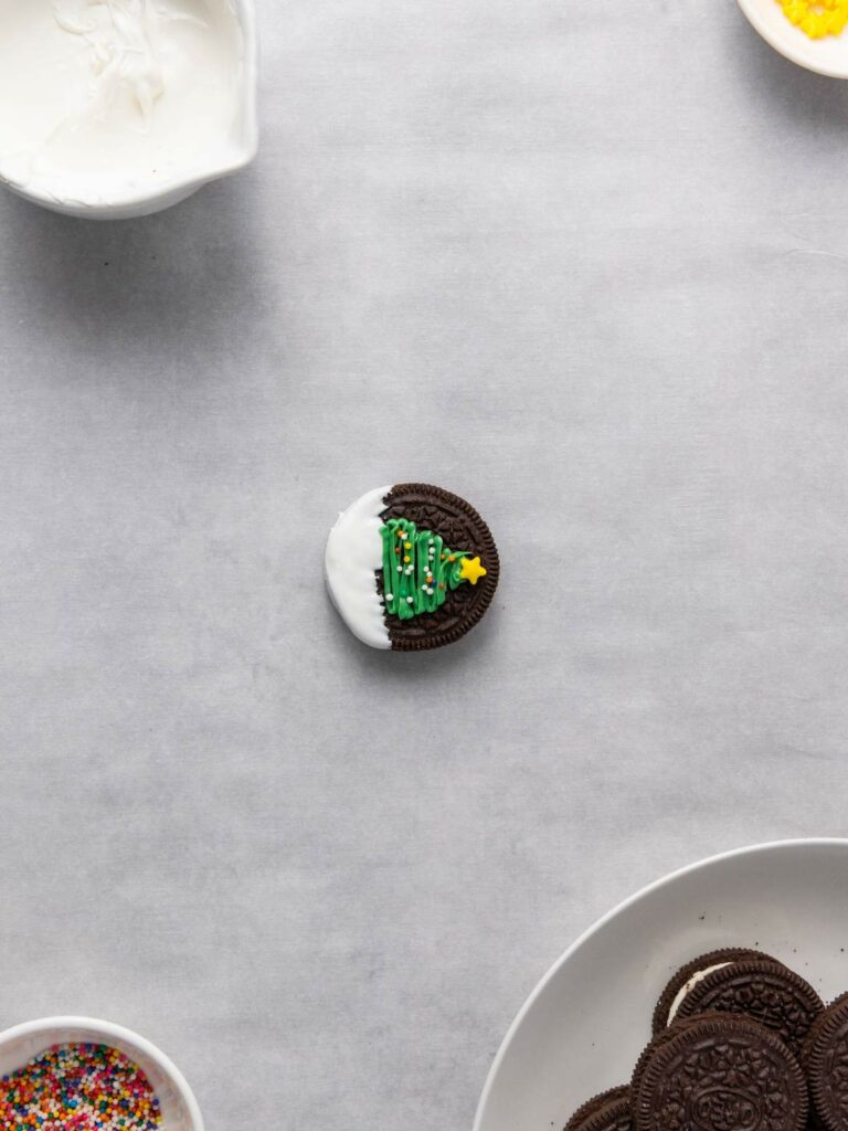 A chocolate sandwich cookie partially dipped in white icing, decorated with a green Christmas tree and a yellow star.