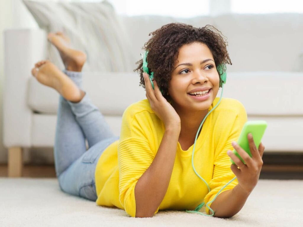 Woman lying on the floor, wearing green headphones and a yellow sweater.