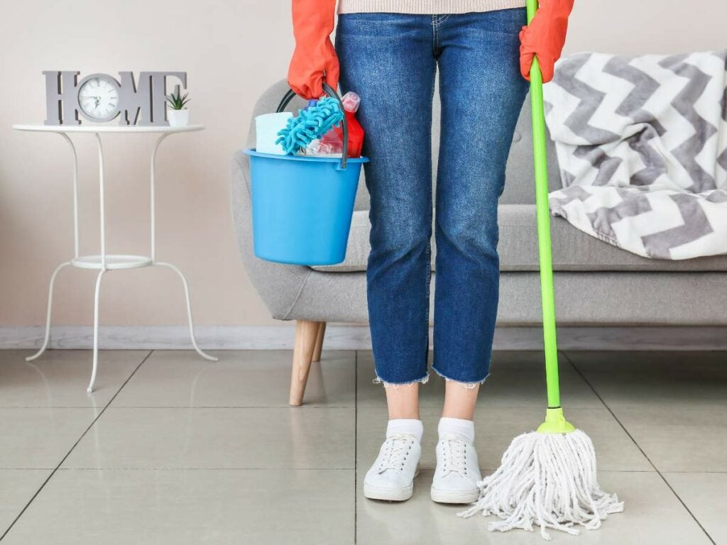 Person holding a blue bucket with cleaning supplies and a mop.