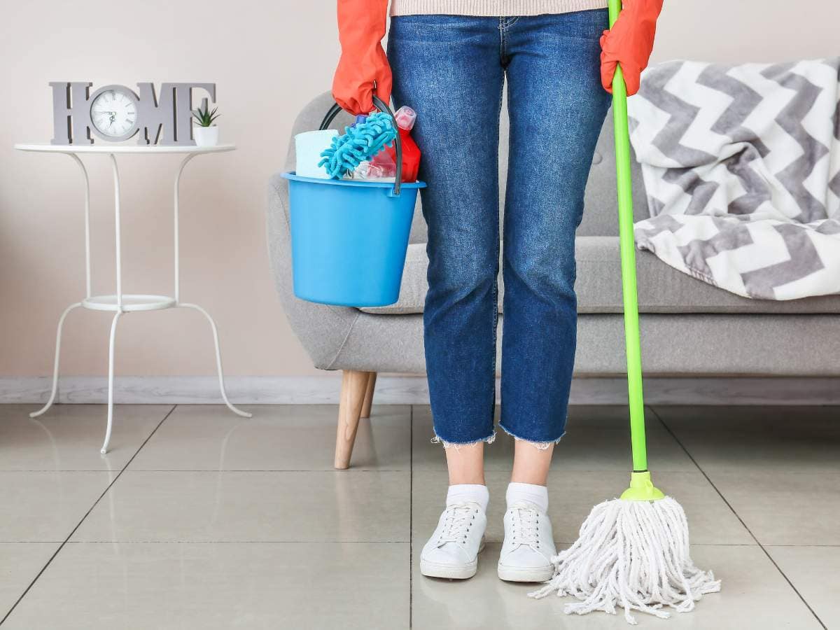 Person holding a blue bucket with cleaning supplies and a mop.